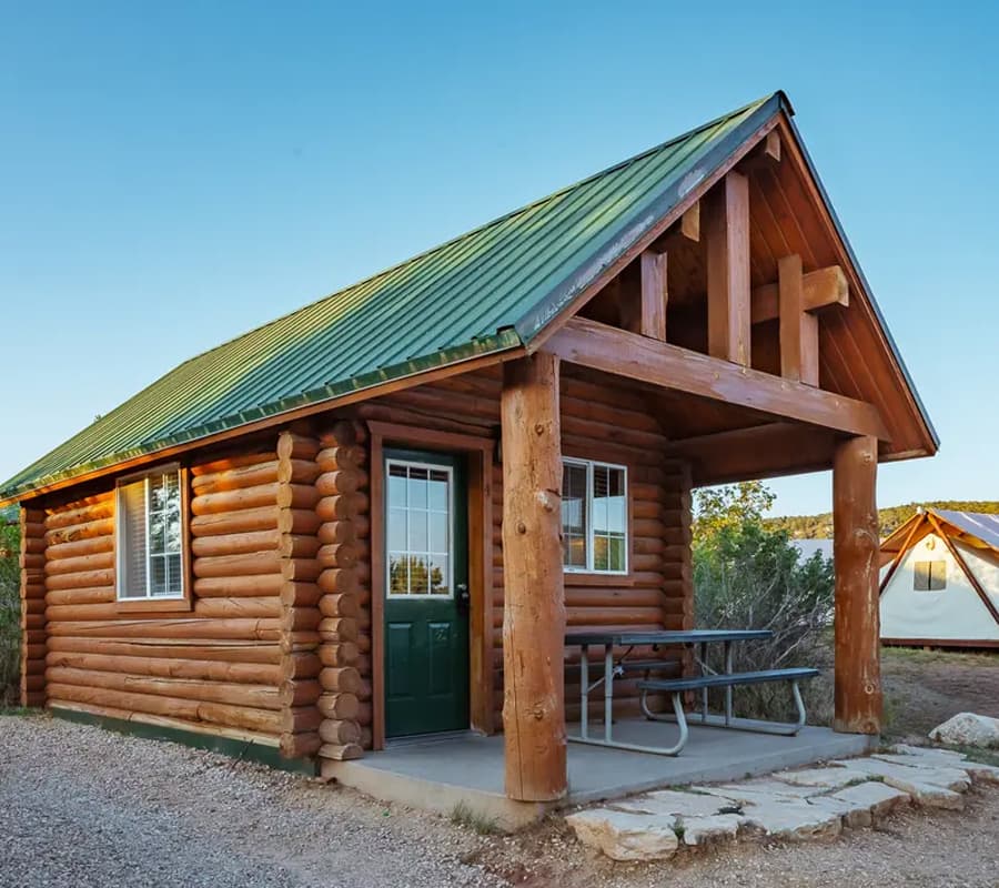 A small log cabin with a green metal roof and a front porch.