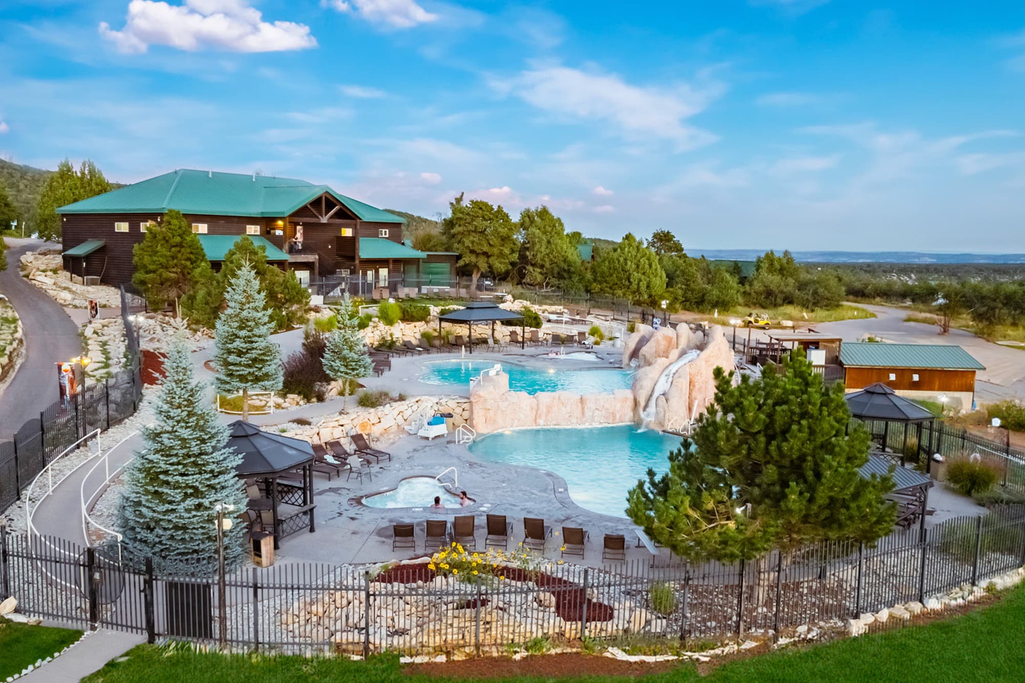 Aerial view of a resort featuring a pool area with rock formations, surrounded by trees and lounge chairs.